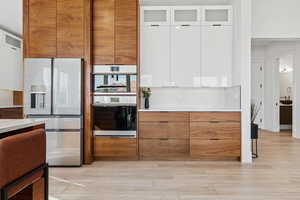 Kitchen with brown cabinets, white cabinetry, stainless steel fridge with ice dispenser, glass insert cabinets, and modern cabinets