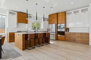 Kitchen featuring brown cabinets, modern cabinets, glass insert cabinets, a breakfast bar, and backsplash