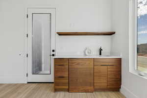 Bar area with brown cabinetry, open shelves, modern cabinets, and light wood-style flooring