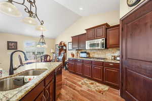 Kitchen featuring hanging light fixtures, lofted ceiling, backsplash, light wood-type flooring, and light stone counters