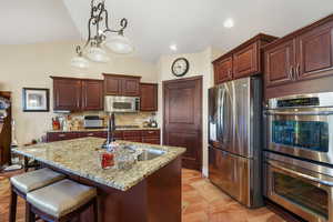Kitchen featuring stainless steel appliances, decorative light fixtures, vaulted ceiling, tasteful backsplash, and light stone counters