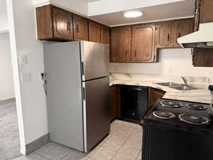 Kitchen with light countertops, black appliances, light tile patterned flooring, and under cabinet range hood