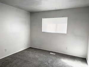 Carpeted spare room featuring a textured ceiling and baseboards