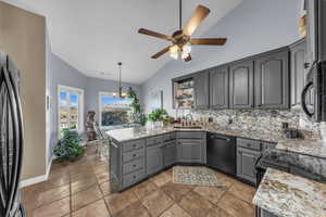 Kitchen with gray cabinetry, a peninsula, tasteful backsplash, black appliances, and stone tile flooring