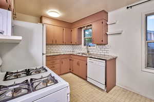 Kitchen with backsplash, white appliances, light floors, and light stone countertops