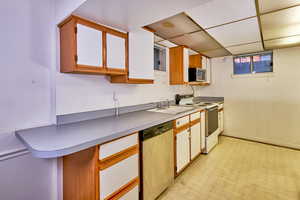Kitchen with brown cabinetry, appliances with stainless steel finishes, a drop ceiling, light flooring, and light countertops
