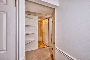 Hallway featuring light carpet and a textured wall