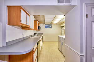 Kitchen featuring brown cabinetry, light floors, white electric stove, light countertops, and a drop ceiling