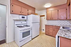 Kitchen featuring light floors, white appliances, and backsplash