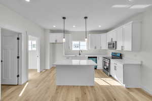 Kitchen featuring appliances with stainless steel finishes, a center island, white cabinets, pendant lighting, and light wood-type flooring