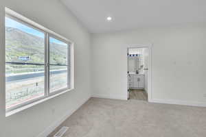 Master bedroom with light carpet, ensuite bath, recessed lighting, and a mountain view