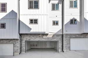 Back of house with stone siding, an attached garage, concrete driveway, and board and batten siding