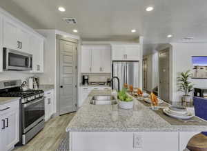 Kitchen featuring stainless steel appliances, white cabinetry, light stone counters, recessed lighting, and a textured ceiling
