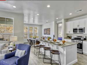 Kitchen with stainless steel appliances, light stone counters, open floor plan, an island with sink, and light wood-type flooring