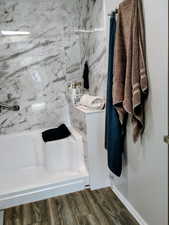 Full bath with a marble finish shower and dark wood-style flooring