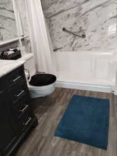 Bathroom with vanity, a marble finish shower, and dark wood-style flooring