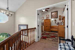 Hallway with lofted ceiling, carpet flooring, an upstairs landing, and a chandelier