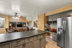 Kitchen featuring stainless steel fridge with ice dispenser, dark countertops, a textured ceiling, decorative backsplash, and open floor plan