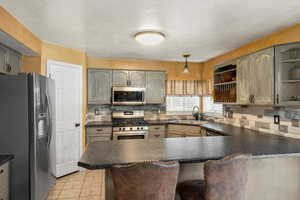 Kitchen featuring appliances with stainless steel finishes, dark countertops, light tile patterned flooring, a peninsula, and a textured ceiling