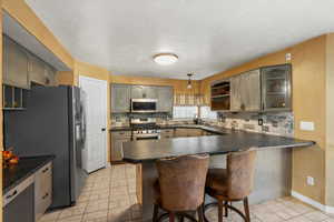 Kitchen with decorative backsplash, appliances with stainless steel finishes, dark countertops, a peninsula, and a textured ceiling