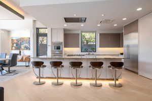 Kitchen featuring a kitchen bar, recessed lighting, light wood finished floors, light stone counters, and stainless steel appliances