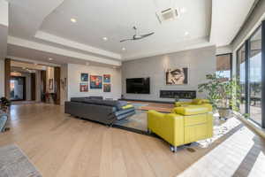 Living room featuring a tray ceiling, plenty of natural light, light wood-style flooring, and recessed lighting