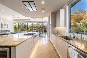 Kitchen with modern cabinets, light stone counters, light wood-style floors, a tray ceiling, and beverage cooler