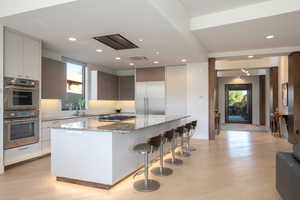 Kitchen with light stone countertops, a center island, a breakfast bar area, appliances with stainless steel finishes, and light wood finished floors