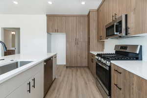 Kitchen with stainless steel appliances, light wood-style flooring, light stone counters, brown cabinets, and recessed lighting