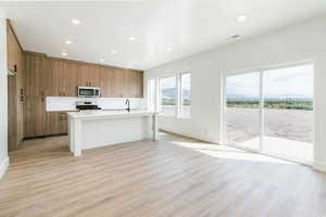Kitchen with brown cabinets, a kitchen island with sink, open floor plan, light wood-type flooring, and modern cabinets