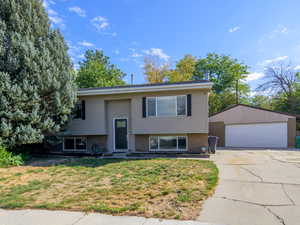 Raised ranch featuring a detached garage, an outbuilding, and a front lawn