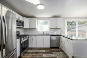 Kitchen with stainless steel appliances, white cabinetry, dark wood-type flooring, and dark stone countertops