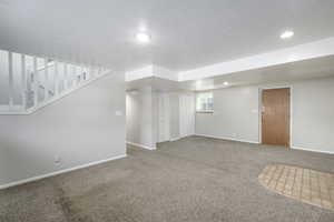 Below grade area with carpet floors, stairs, and a textured ceiling