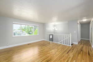 Empty room with light wood finished floors, a textured ceiling, and a chandelier