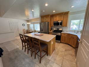 Kitchen featuring appliances with stainless steel finishes, brown cabinets, a textured ceiling, a center island, and light countertops