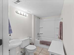 Full bathroom featuring  shower combination, a textured ceiling, and light tile patterned flooring