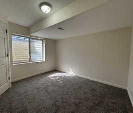 Carpeted spare room featuring a textured ceiling and baseboards