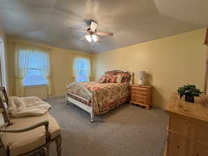 Bedroom featuring a textured ceiling, light colored carpet, lofted ceiling, and ceiling fan