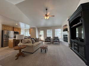 Living room featuring a fireplace, light colored carpet, a ceiling fan, vaulted ceiling, and a textured ceiling