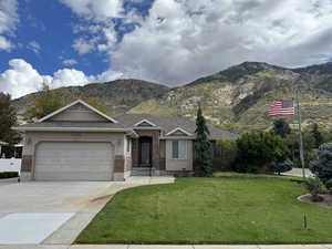Ranch-style house with driveway, a front lawn, a mountain view, an attached garage, and brick siding