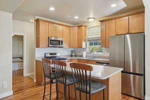 Kitchen with appliances with stainless steel finishes, light wood finished floors, a kitchen island, a kitchen breakfast bar, and backsplash