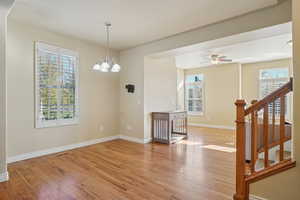 Unfurnished dining area featuring light wood finished floors, a chandelier, stairs, and a ceiling fan