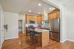 Kitchen featuring appliances with stainless steel finishes, a breakfast bar, recessed lighting, light wood-style floors, and a center island
