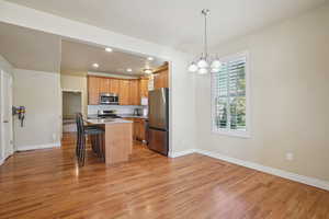Kitchen featuring a breakfast bar, pendant lighting, appliances with stainless steel finishes, a center island, and light wood-style floors