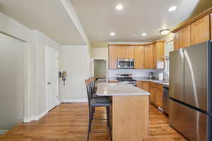 Kitchen with stainless steel appliances, light wood-style floors, a center island, a kitchen breakfast bar, and recessed lighting