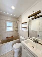 Bathroom with tile walls, vanity, light tile patterned flooring, and tiled shower / bath combo
