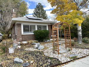 View of front facade featuring solar panels, a chimney, and brick siding