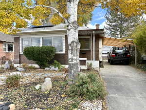 View of front of home featuring brick siding, a chimney, driveway, and solar panels