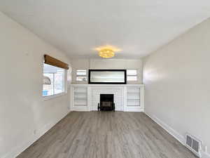 Unfurnished living room with wood finished floors and a brick fireplace