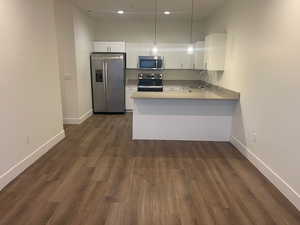 Kitchen with appliances with stainless steel finishes, white cabinetry, hanging light fixtures, a peninsula, and dark wood-type flooring